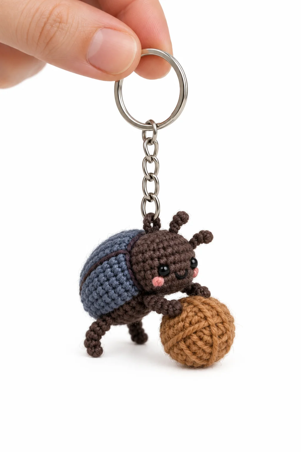 Crochet dung beetle keychain with a blue shell pushing a ball of brown yarn on a silver keyring