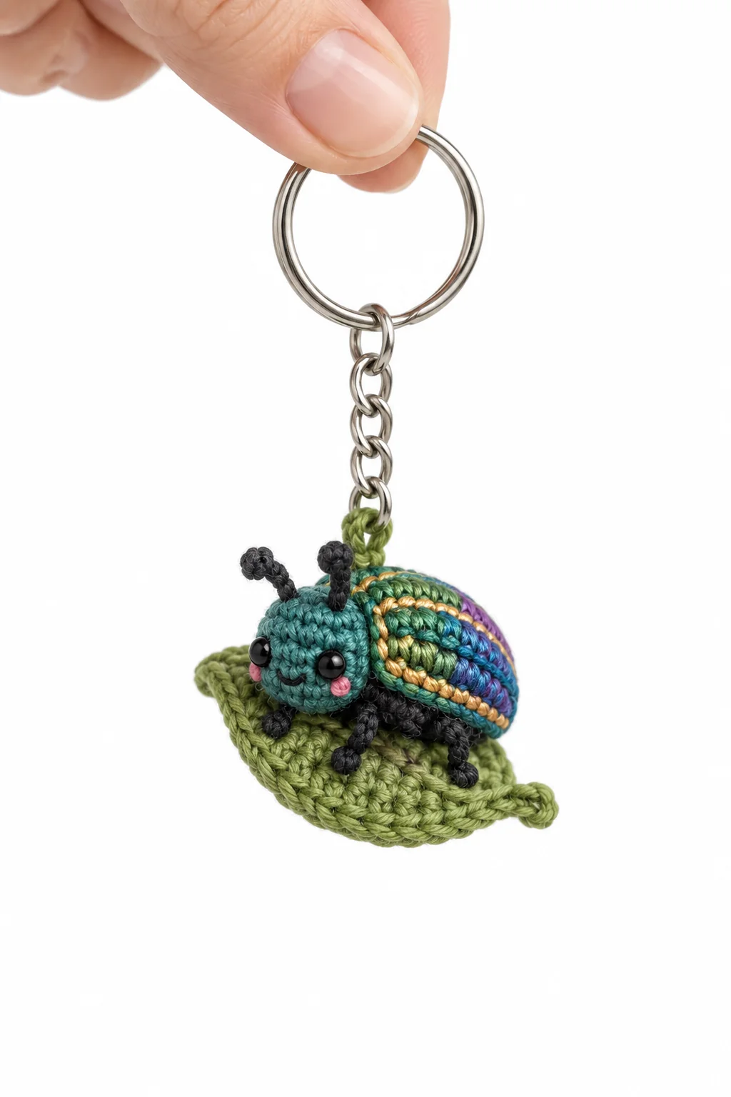 Crochet ladybug keychain with an iridescent blue-green-purple shell sitting on a green leaf